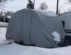 A vehicle fitted with the Ultimate Toys Trailer Cover by PahaQue from Paha Que Custom stands in a snowy lot, snow gathered on top and around it. Winter trees and a utility pole appear in the background.
