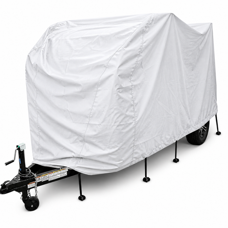 A small trailer is protected with the Ultimate Toys Trailer Cover by PahaQue, featuring durable weather-resistant material by Paha Que Custom, standing on four stabilizing jacks with a black hitch and jack visible at the front.