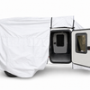 A small trailer is partially covered with the Encore Trailer Cover by Paha Que Custom, offering premium protection. The open side door reveals a dark interior with black trim, a window in the door, and visible off-road tires.