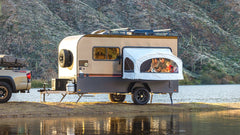 A family enjoys lake and mountain views from inside the weatherproof Toy Hauler Patio Ramp Tent by PahaQue for Intech Trailers, while their truck is parked beside the camper.