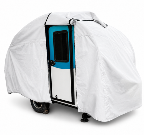 A small trailer with a blue and white door is protected by the Helio O Series Trailer Cover by PahaQue Heavy Duty MagnaTuf Protection, exposing only the door and one wheel. The custom fit cover by Paha Que Custom stands out on a white background.