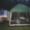 A small silver teardrop camper is parked beside a Paha Que Custom 5x7 Trailer Side Tent Screen Room for Camping and Outdoor Adventures, featuring two chairs and a table inside, surrounded by trees at dusk.