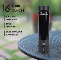 A black Cauldryn Coffee Pro by PahaQue Wilderness sits on an outdoor metal table. Its digital base shows the temperature. Features: 16oz, vacuum insulated, spill-proof lid, easy to clean (hand wash only).