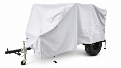 A small trailer fitted with the white Sherpa Trailer Cover by PahaQue Wilderness displays its black wheels and towing hitch, with a support wheel visible at the front.