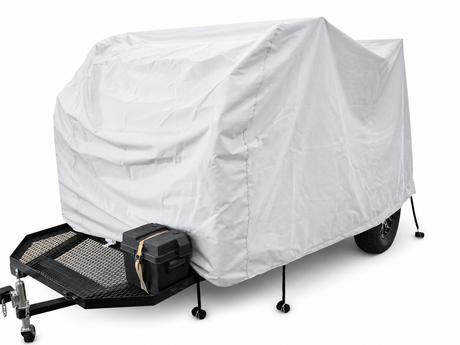 A UKAN Camp 590G/585G 5x9 utility trailer by PahaQue Wilderness features a white custom-fit cover for protection, black metal frame, front storage box, and four stabilizing legs, parked on a flat surface.