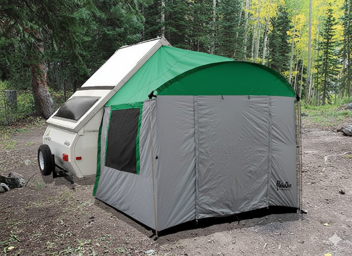 A Paha Que Custom A-Frame Trailer Side Tent, designed for Aliner, Chalet, Rockwood, and Jayco 12 & 15 box trailers, is set up at a wooded campsite with a pop-up camper surrounded by trees and dirt ground.