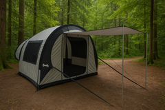 A spacious gray and black Paha Que Custom NuCamp TAB 360 Trailer Side Tent for Enhanced Camping Experience, with an extended canopy and open door, stands in a lush green forest clearing surrounded by tall trees.