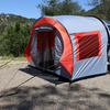 A Paha Que Custom NuCamp TAB 320 Trailer Side Tent for TAB and Boondock Trailers is attached to a camper on gravel, surrounded by trees and hills under a clear blue sky.