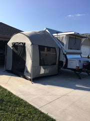 A Paha Que Custom A-Frame Trailer Side Tent for Aliner, Chalet, Rockwood, and Jayco 12 and 15 box trailers is set up on a driveway beside a house, its attached screened area providing extra space under the clear sky.