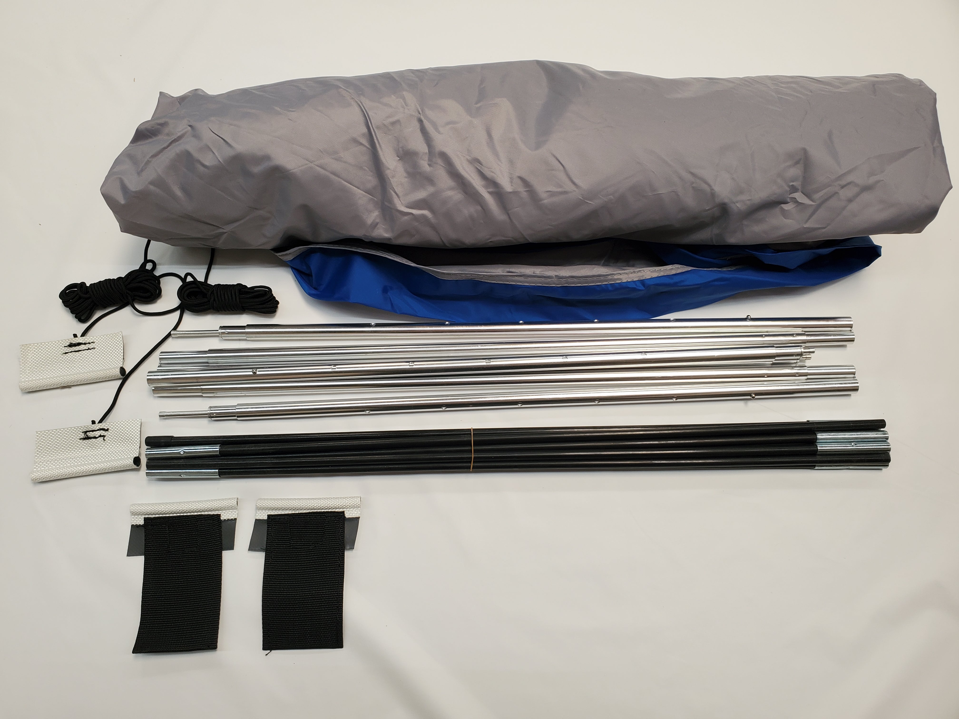 A disassembled Paha Que Custom R Pod Trailer Visor kit on a white surface, showing rolled fabric, metal poles, straps, and cords—perfect for anyone seeking premium R Pod accessories.