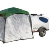 A compact white teardrop camper displays the Paha Que Custom 5x7 Trailer Side Tent Screen Room in green and silver at its entrance, adding extra space for relaxing or storage, all set against a plain white background.