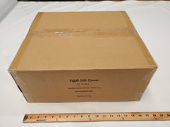 A sealed cardboard box labeled NuCamp TAB 360 CS (Clamshell) Trailer Cover by PahaQue sits on a white surface beside a wooden ruler. This Paha Que Custom product features heavy-duty, weatherproof protection and comes in a box about 24 inches long.